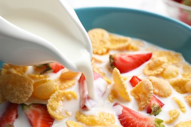 Pouring milk into bowl with crispy corn flakes and strawberries, closeup