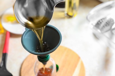 Pouring used cooking oil into bottle through funnel in kitchen, closeup