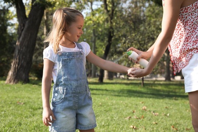 Mother applying insect repellent onto girl's hand in park