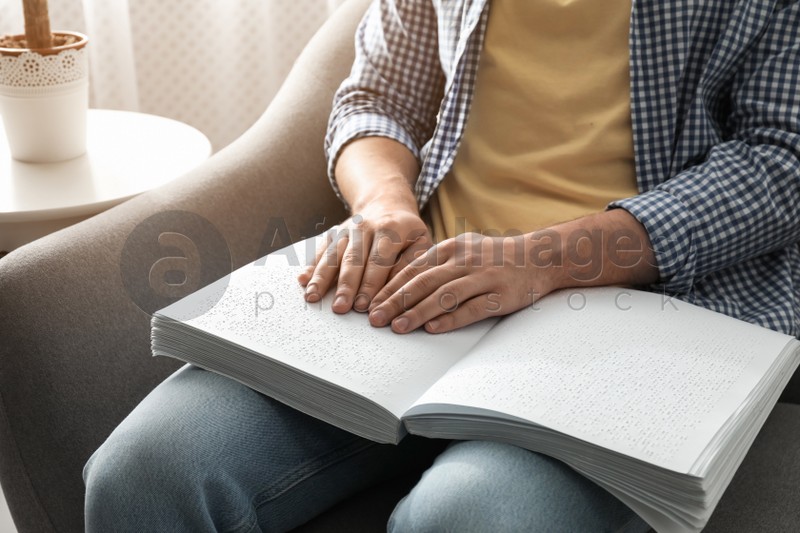 Blind man reading book written in Braille on sofa, closeup