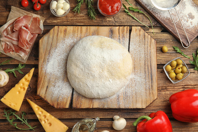Flat lay composition with dough and fresh ingredients for pizza on wooden table