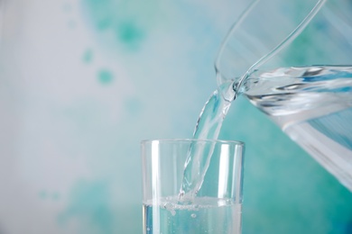 Pouring water from jug into glass on color background, closeup. Space for text