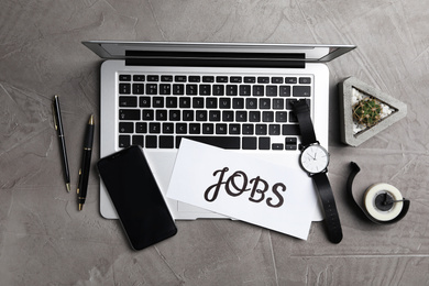 Flat lay composition with word JOBS, laptop and smartphone on grey table. Career concept