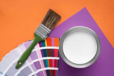 Photo of Can with white paint, color palette and brush on color background, flat lay