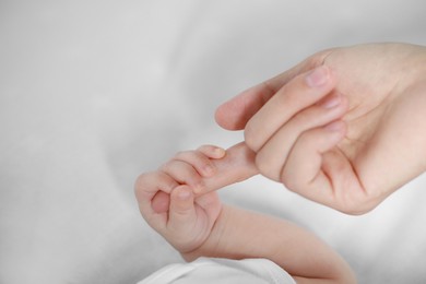 Photo of Baby holding motherʼs hand on bed, closeup