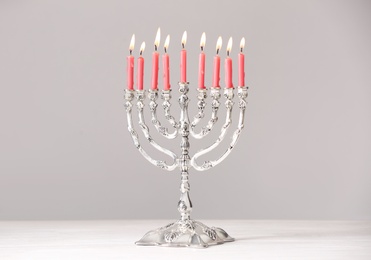 Silver menorah with burning candles on table against light grey background. Hanukkah celebration