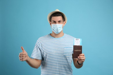 Male tourist in protective mask holding passport with ticket on turquoise background