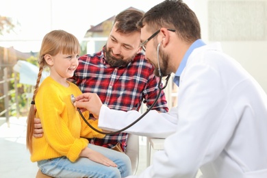 Photo of Children's doctor examining little girl with stethoscope in hospital