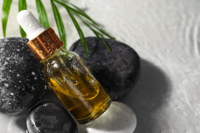 Bottle of face serum, spa stones and leaf in water on light background, closeup