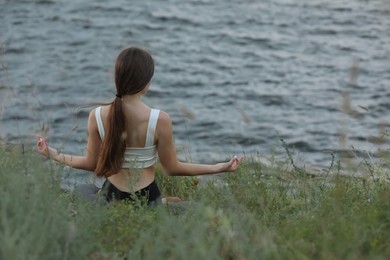 Teenage girl meditating near river, back view. Space for text