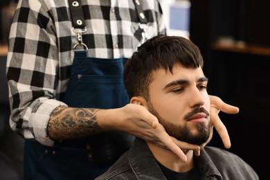 Professional hairdresser working with bearded client in barbershop