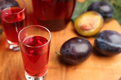 Delicious plum liquor in shot glass on wooden board. Homemade strong alcoholic beverage
