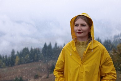 Young woman in raincoat enjoying mountain landscape under rain