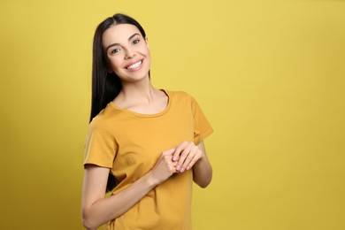 Portrait of happy young woman with beautiful black hair and charming smile on yellow background, space for text
