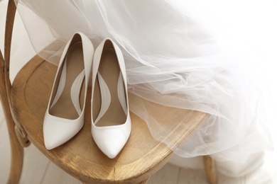 Pair of white wedding high heel shoes and veil on wooden chair indoors