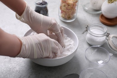 Photo of Woman in gloves making bath bomb mixture at grey table, closeup