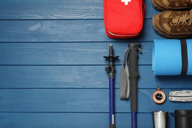 Flat lay composition with trekking poles and other hiking equipment on blue wooden background, space for text