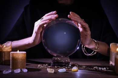 Photo of Soothsayer using crystal ball to predict future at table in darkness, closeup. Fortune telling