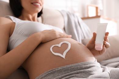 Young pregnant woman with cosmetic product on sofa indoors, closeup