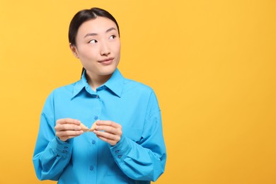 Photo of Asian woman breaking tasty fortune cookie with prediction on yellow background, space for text