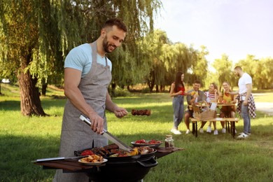 Photo of Man cooking meat and vegetables on barbecue grill in park