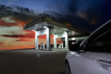 Car driving up to modern gas filling station beside the road in evening