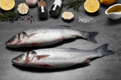 Fresh raw sea bass fish, seasonings and lemons on black table