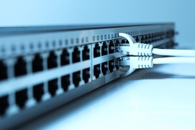 Photo of Closeup view of network switch with cables on light background, toned in blue. Internet connection