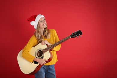 Young woman in Santa hat acoustic guitar on red background, space for text. Christmas music
