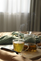 Photo of Wooden tray with freshly brewed tea on bed in room. Cozy home atmosphere