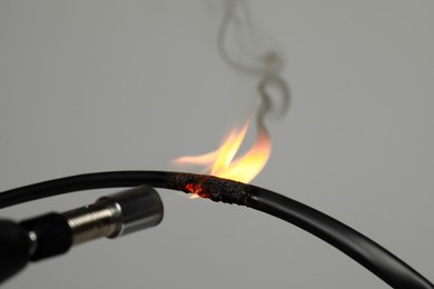 Photo of Inflamed black wire on grey background, closeup. Electrical short circuit