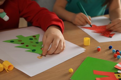 Little children making beautiful Christmas greeting cards at wooden table, closeup