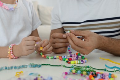Father with his daughter making beaded jewelry at table, closeup