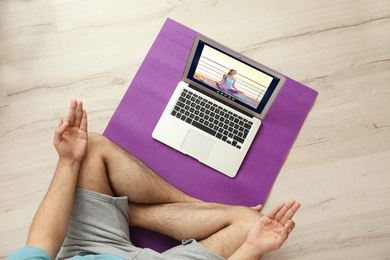 Distance yoga course during coronavirus pandemic. Man having online practice with instructor via laptop at home, top view