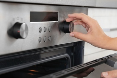 Photo of Woman regulating cooking mode on oven panel, closeup