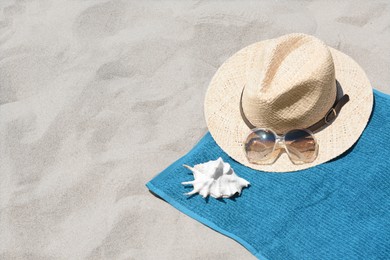 Photo of Soft blue towel, sunglasses, straw hat and seashell on sandy beach, space for text