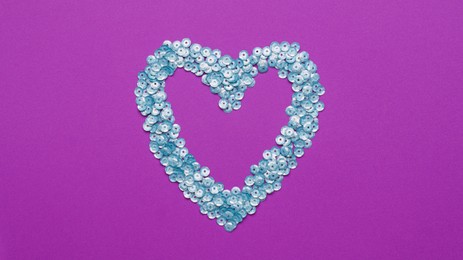 Heart made of silver sequins on purple background, top view