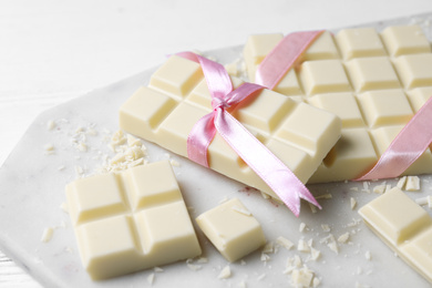 Tasty white chocolate with ribbons on marble board, closeup