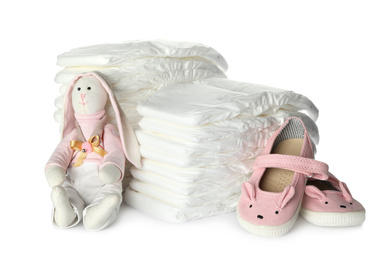 Disposable diapers, toy bunny and child's shoes on white background