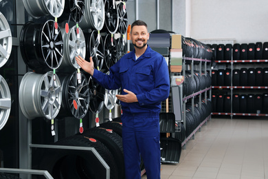 Male mechanic near car tires and alloy wheels in auto store