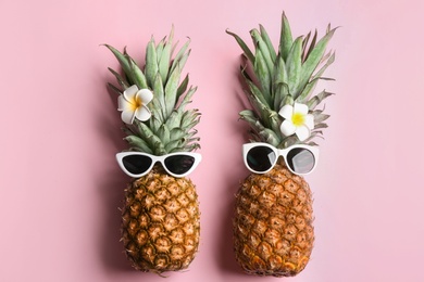 Photo of Funny pineapples with sunglasses and plumeria flowers on pink background, flat lay. Creative concept