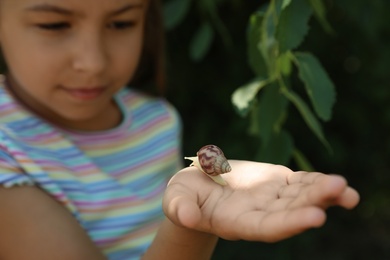 Photo of Girl playing with cute snail outdoors, focus on hand. Child spending time in nature