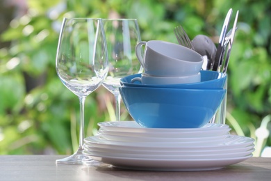 Clean dishes, cups, shiny cutlery and glasses on wooden table against blurred background