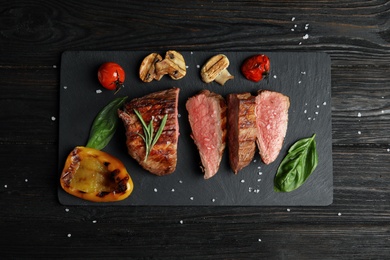 Board with slices of grilled meat on black wooden table, top view