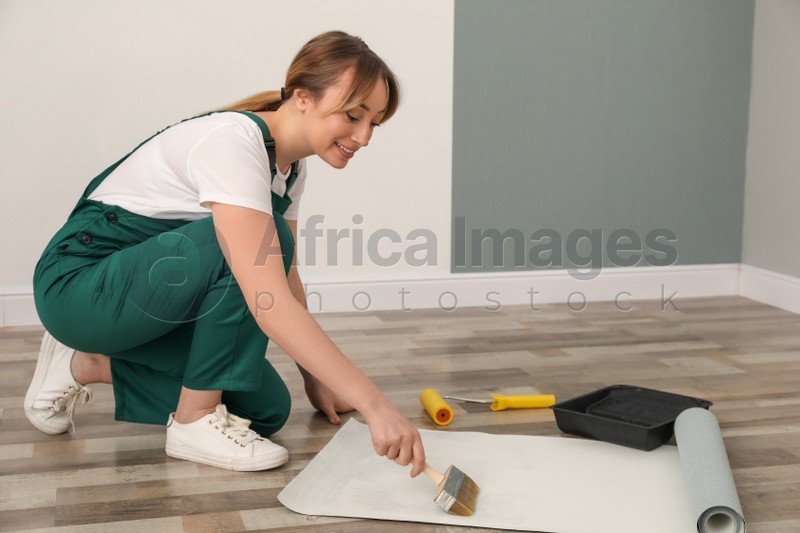 Photo of Worker applying glue onto wall paper sheet on floor indoors