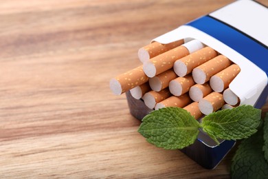 Pack of menthol cigarettes and mint leaves on wooden table, closeup. Space for text
