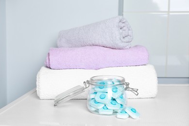 Jar with water softener tablets near stacked towels on white table