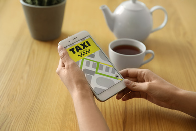 Woman ordering taxi with smartphone at wooden table, closeup