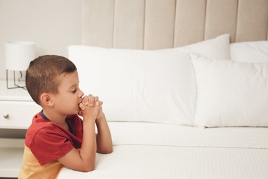 Cute little boy with hands clasped together saying bedtime prayer at home. Space for text