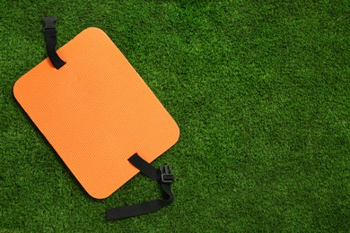 Orange foam tourist seat mat on green grass, top view. Space for text